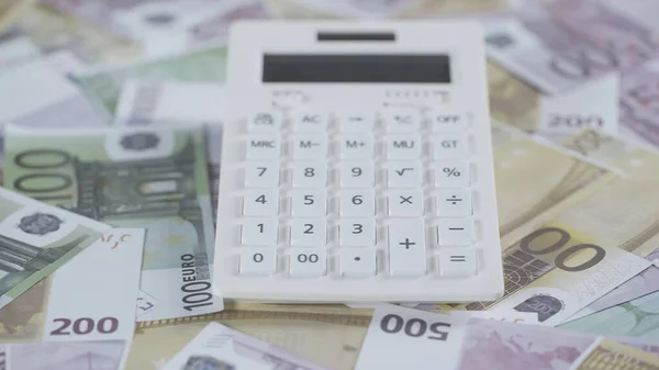 White calculator on scattered euro banknotes in studio — стоковое фото