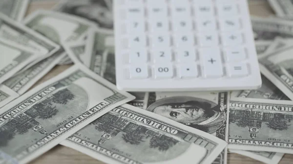 Close up of white calculator on scattered dollar banknotes on wooden table — Stock Photo