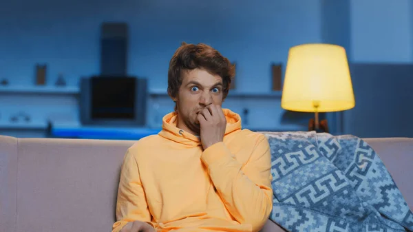 Scared young man in yellow hoodie watching movie in living room — Stockfoto