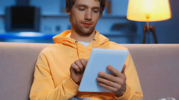 Молодий чоловік в жовтому светрі використовує цифровий планшет у вітальні — стокове фото