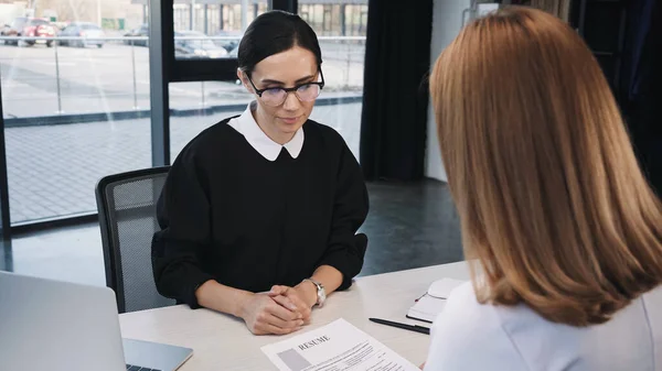 Woman holding resume near businesswoman in eyeglasses during job interview — Stock Photo