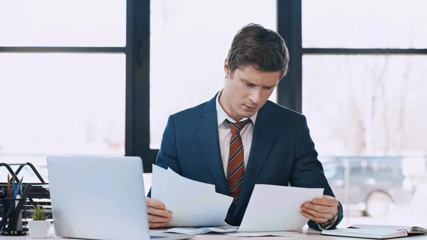 Thoughtful businessman working with documents near laptop in office — Stockfoto