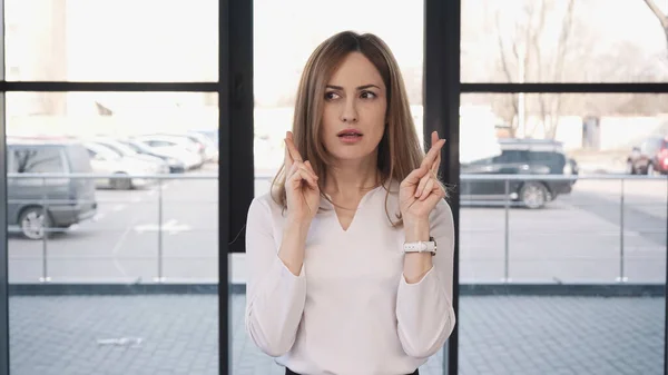 Worried woman holding crossed fingers before job interview in office — Fotografia de Stock