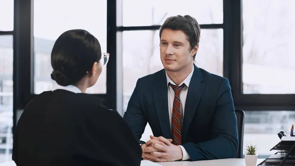 Smiling businessman sitting with clenched hands while listening to woman on job interview — Stock Photo