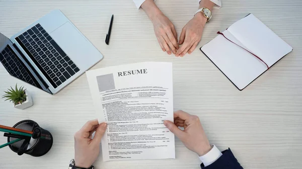 Top view of cropped businessman with resume near woman and laptop on desk — стоковое фото