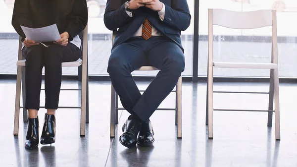 Cropped view of woman with resume waiting for job interview near man in office — Stock Photo