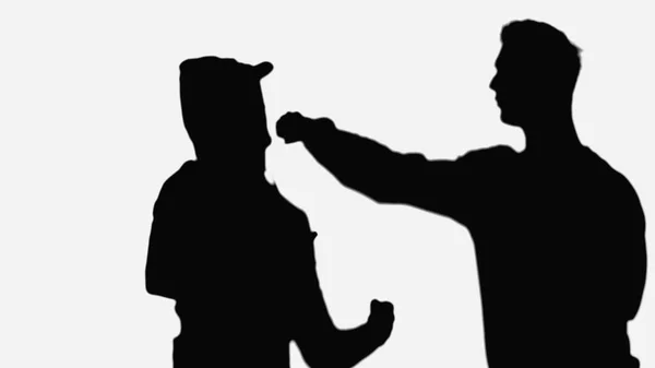 Silhouette of man punching criminal man in cap and hood isolated on white — Stock Photo