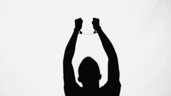 Silhouette of criminal man with handcuffs on raised hands isolated on white — Stock Photo