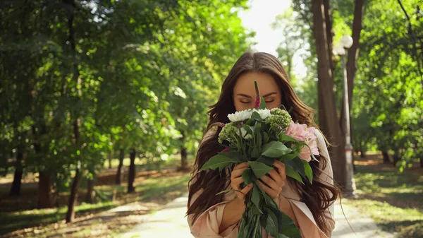 Brunette woman smelling bouquet of flowers in green park — Stock Photo