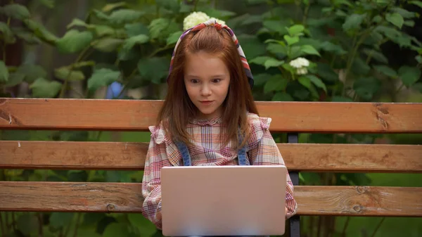 Amazed redhead kid using laptop on bench in park — Stock Photo