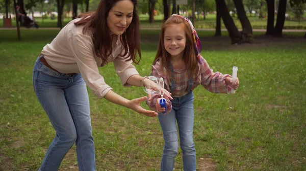 Smiling parent and girl holding soap bubbles in summer park — Stock Photo