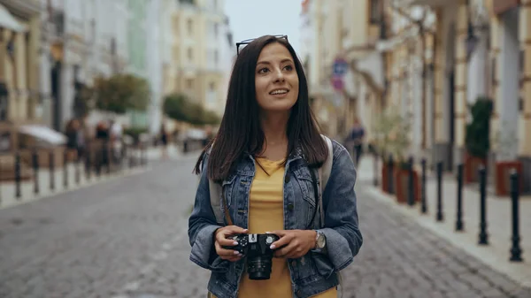 Cheerful tourist holding vintage camera on urban street - foto de stock