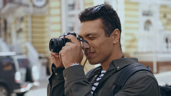 Bi-racial traveler taking photo on film camera on street - foto de stock