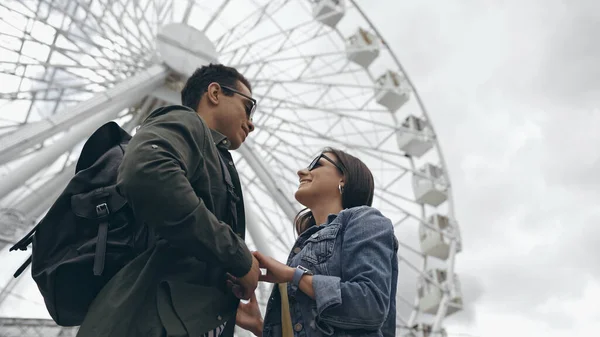 Low angle view of multiethnic tourists holding hands near blurred ferris wheel — Foto stock