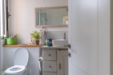 Ahşap tezgahta beyaz lavabo ve üzerinde bir ayna asılı. Banyo içi..