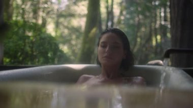 Yağmur sırasında bir ormanda küvette bir kız. Lüks bir kaplıcada tropikal yağmur ormanlarında banyoda dinlenen genç ve güzel bir kadın.