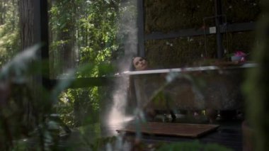 A girl in a bathtub in a forest during the rain. Beautiful young woman relaxing in the bathroom in the tropical rainforest jungle in a luxury spa while raining