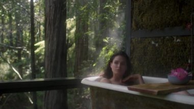 Yağmur sırasında bir ormanda küvette bir kız. Lüks bir kaplıcada tropikal yağmur ormanlarında banyoda dinlenen genç ve güzel bir kadın.