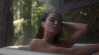 Yağmur sırasında bir ormanda küvette bir kız. Lüks bir kaplıcada tropikal yağmur ormanlarında banyoda dinlenen genç ve güzel bir kadın.