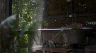 Yağmur sırasında bir ormanda küvette bir kız. Lüks bir kaplıcada tropikal yağmur ormanlarında banyoda dinlenen genç ve güzel bir kadın.