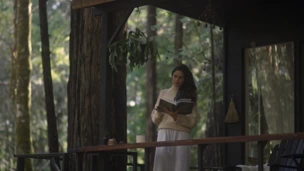 Young Woman Reading Book Drinking Hot Tea Porch Cozy Cabin Stockvideo