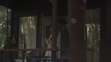 Kitap okuyan ve ormandaki sıcak bir kulübede sıcak çay içen genç bir kadın. Ormanın ortasındaki ahşap kulübe güneşli ahşap dağ kulübesi kırsal ev mimarisi..