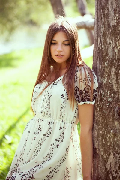 Menina em um vestido de verão apoiando-se em uma árvore velha — Fotografia de Stock