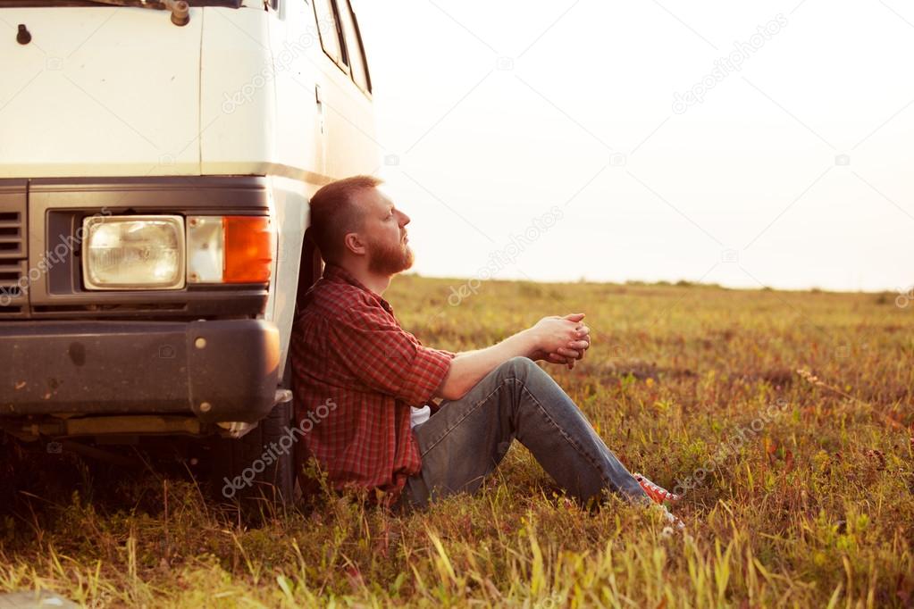Driver resting in a field near his car