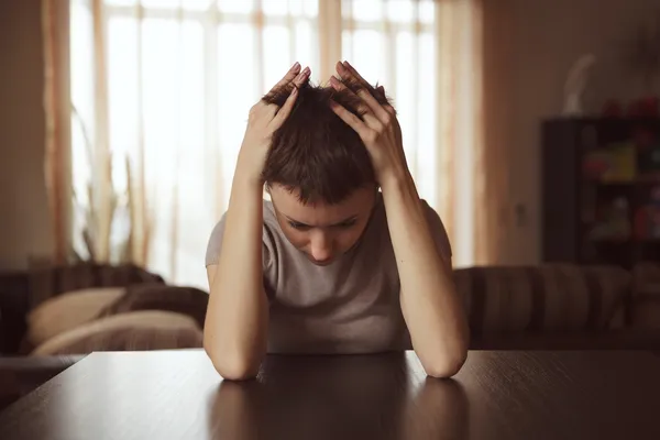 Young woman sitting hugging her head — Stock Photo, Image