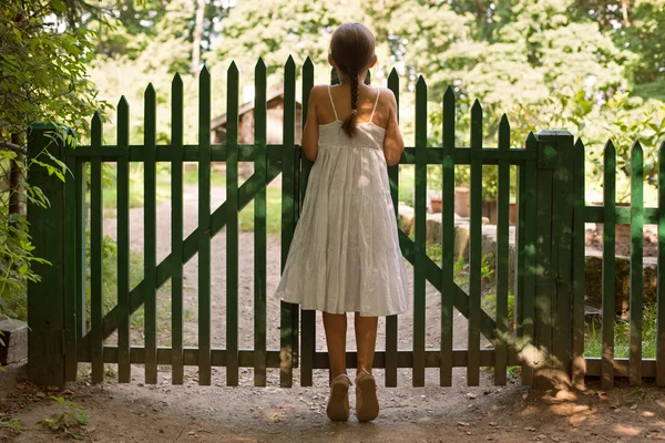Girl standing on tiptoes and looking over the fence — Stock Photo, Image