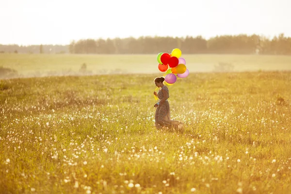 Jovem mulher feliz com balões em um campo — Fotografia de Stock