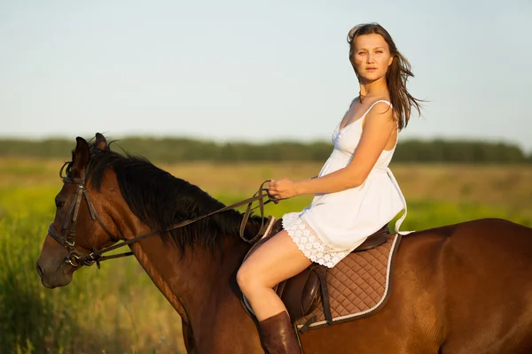 Menina em vestido montando em um cavalo marrom — Fotografia de Stock