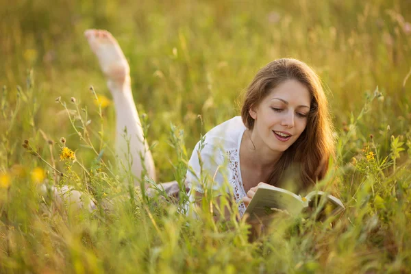Glad kvinna ligga på gräset och läsa en bok — Stockfoto