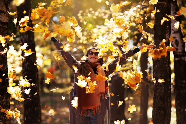 美しい若い女性が秋の晴れた日にカエデの葉を投げます — ストック写真