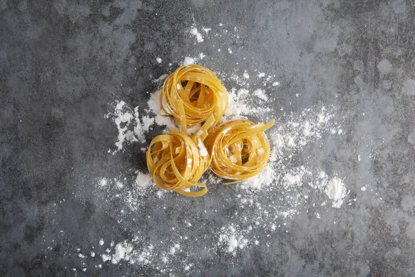Three balls of rolled spaghetti in flour lie on a gray table