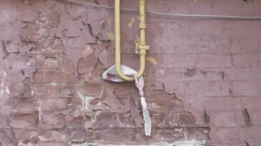Evin ön cephesinde eski bir tuğla duvar, soyulmuş boya, eski püskü sarı bir gaz borusu ve kullanılmış bir paket. Yakın çekim, dikey döndürme.
