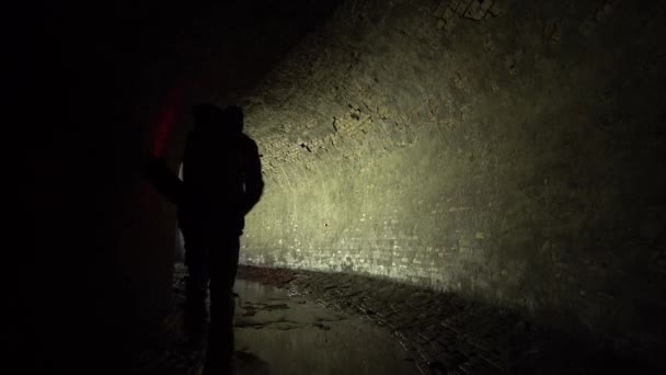 赤い提灯を持った男が19世紀の古いレンガ造りの地下排水溝のコレクターの中を歩く — ストック動画