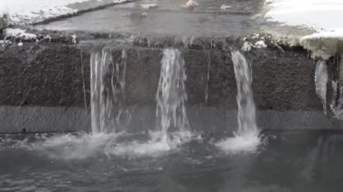Small artificial waterfall in a concrete drainage canal with steam in winter.