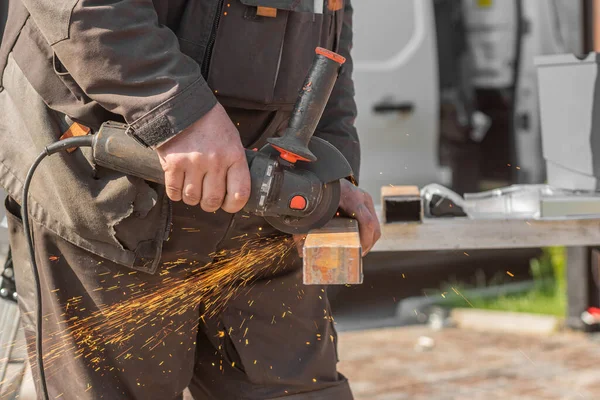 An worker saws a metal beam with an angle grinder with sparks.