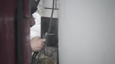 Kaynakçı inşaat alanındaki bir duvara metal bir yapı kaynak yapar, atölyede, etraflarındaki kıvılcımlar uçuşurken, koruyucu bir kask ve ekipman giyerler..