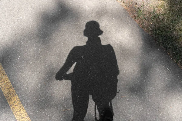 Shadow silhouette of a tourist on the asphalt on the road in the woods.