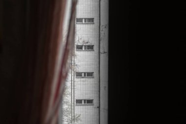 A view from a dark window on a vertical row of narrow windows in a modernist high-rise building.