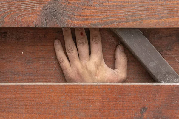 A creepy person\'s hand is trapped between boards and metalwork, an accident at work.