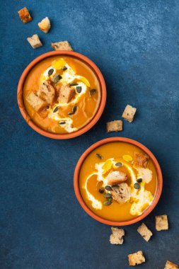Kremalı ve kızarmış ekmekli balkabağı kremalı çorba hazır. Mavi arka plan manzaralı iki porsiyon.