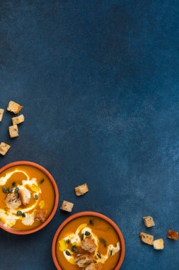 Kremalı ve kızarmış ekmekli balkabağı kremalı çorba hazır. Mavi arka plan manzaralı iki porsiyon.