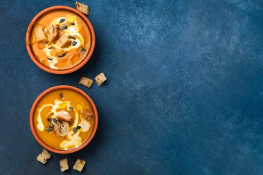 Kremalı ve kızarmış ekmekli balkabağı kremalı çorba hazır. Mavi arka plan manzaralı iki porsiyon.