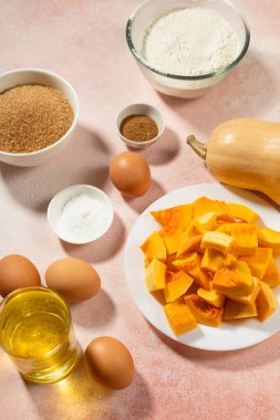 Pembe masadaki kaselerde balkabağı turtası malzemeleri.