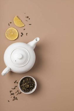 Fincanda yeşil çay ve bej arka planda limon olan beyaz çaydanlık.