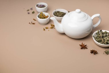 Beyaz çaydanlık ve bej arka planda farklı çay çeşitleri.