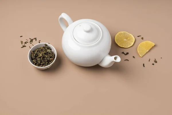 Fincanda yeşil çay ve bej arka planda limon olan beyaz çaydanlık.